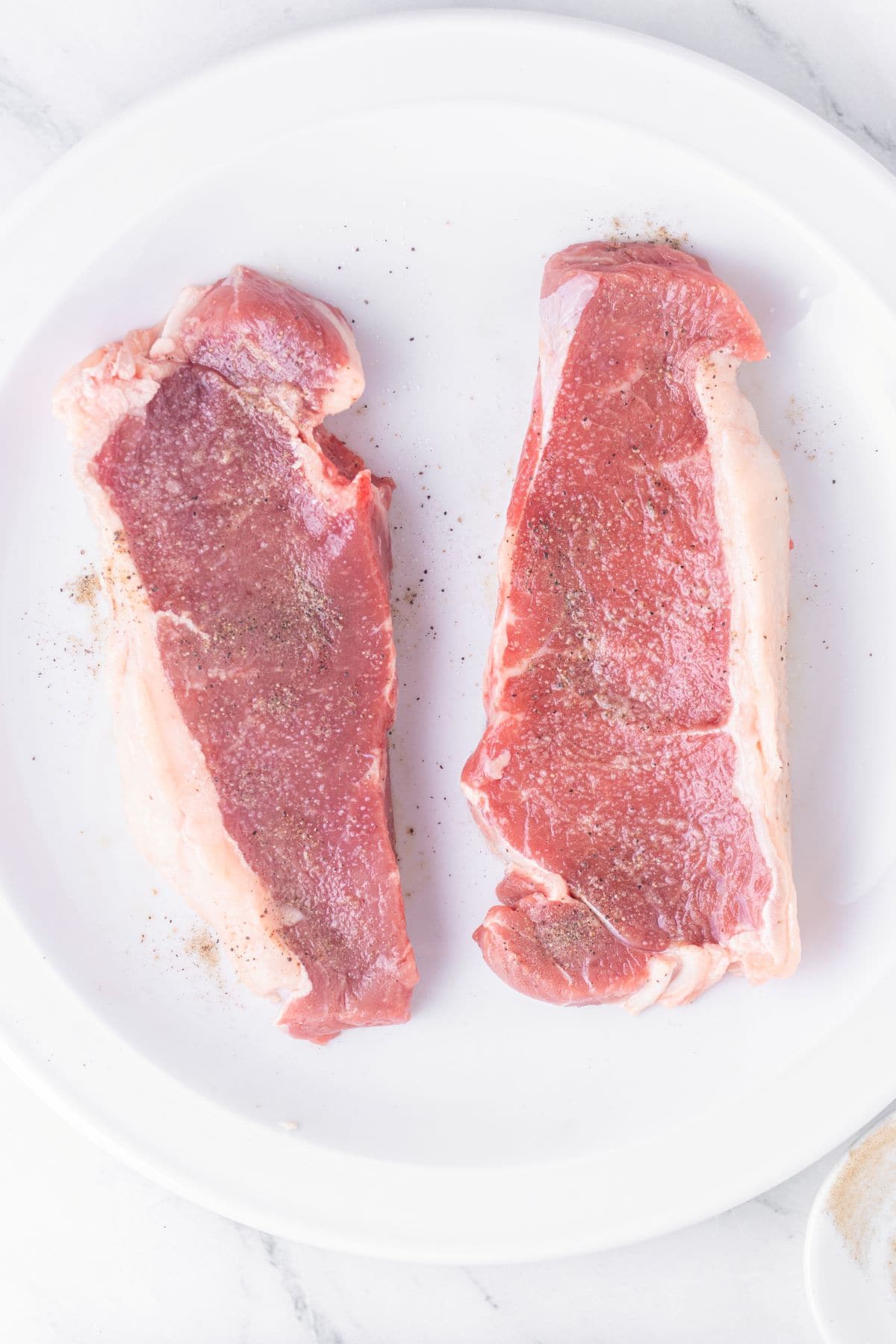Seasoning steaks with salt and pepper.