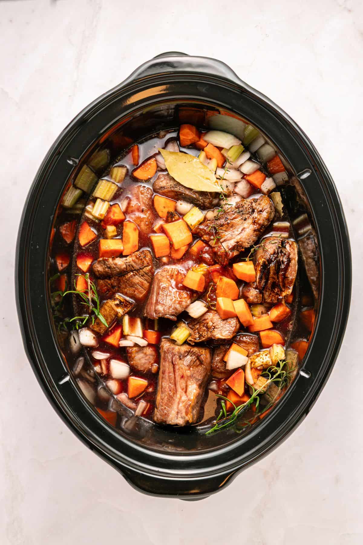 Adding seared beef short ribs to the slow cooker.